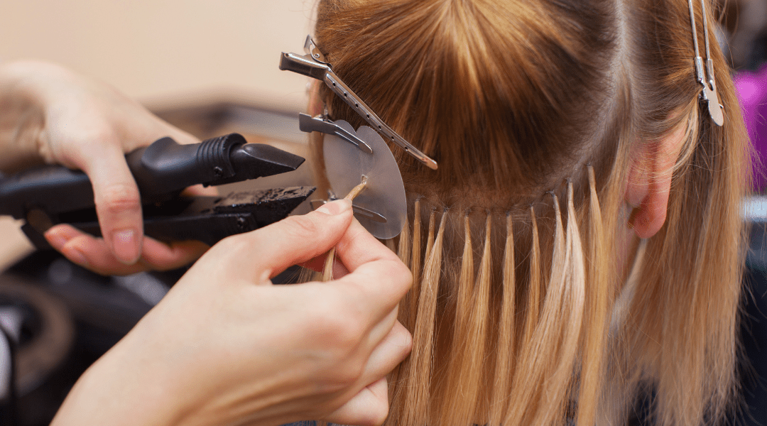 Hairdresser applying luxury hair extensions to a blonde client in a beauty salon.