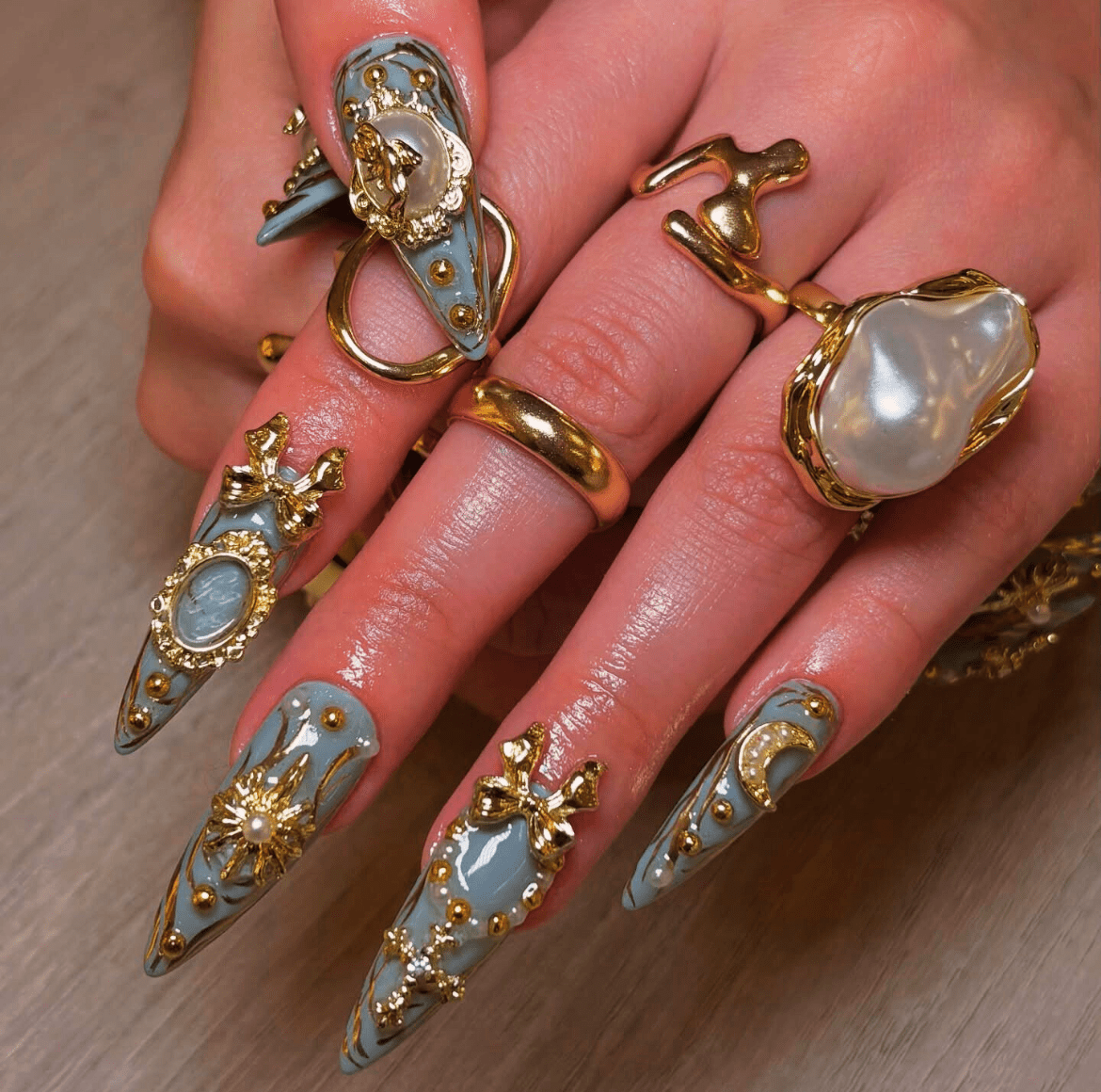 3D Pattern Nail Art with long pastel blue nails featuring gold and white accents, including beads, bows, and intricate details for a luxurious, gothic design