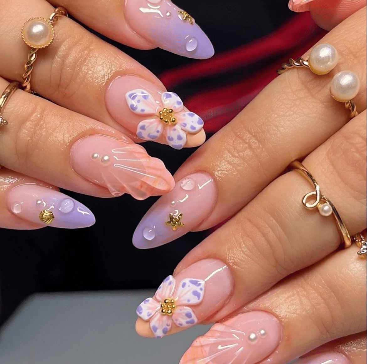 Pink to lavender gradient nails with 3D floral gel art, adorned with pearls and gold rings featuring pearl accents.
