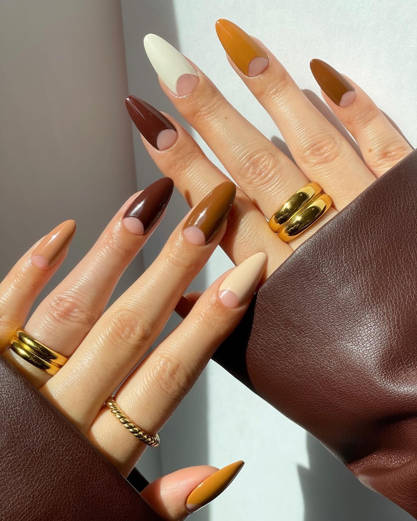 Brown French tip nails with beige base and dark half moon accents, styled with gold rings and leather cuff