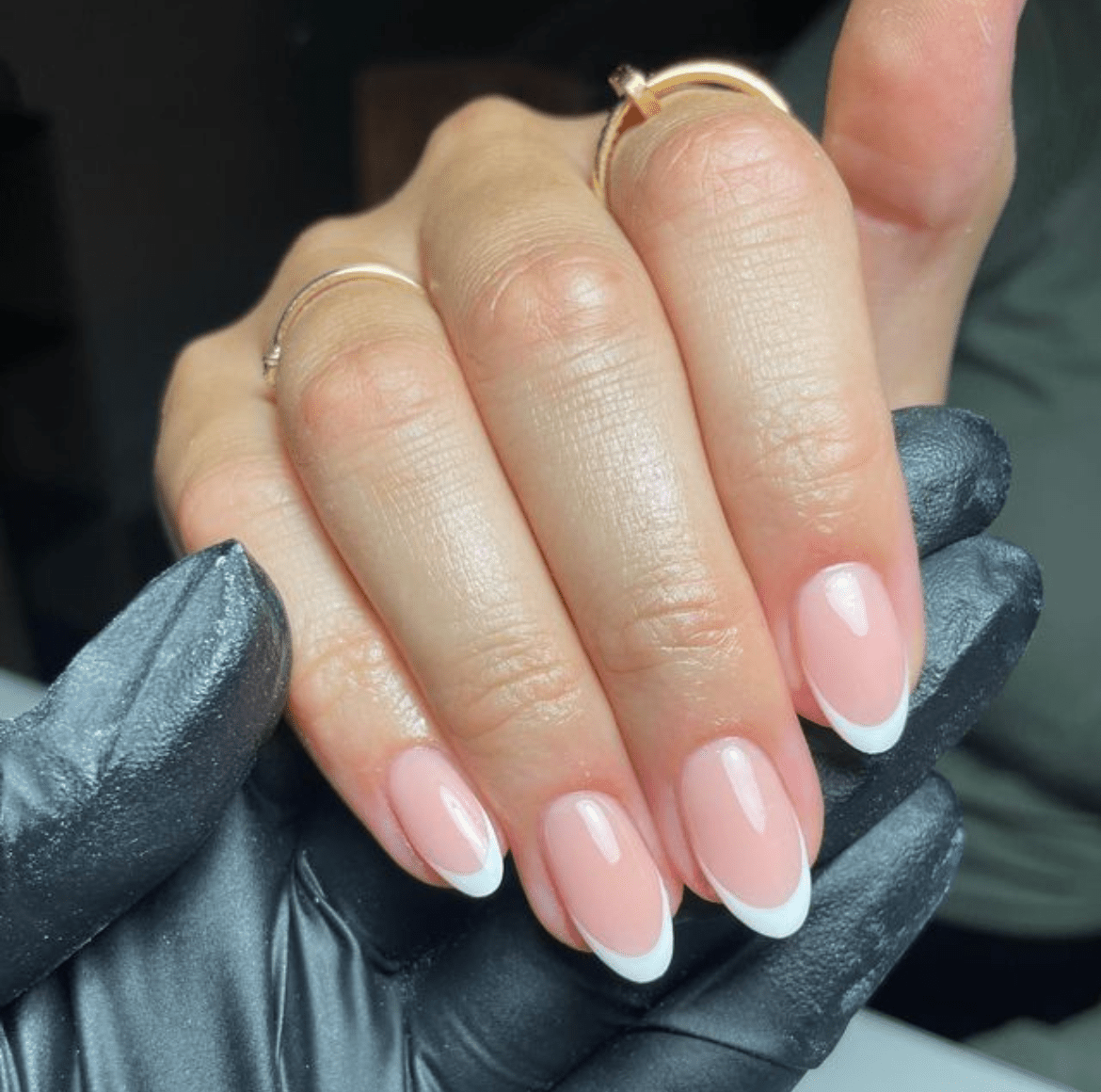 Close-up of almond-shaped nails with a classic French manicure on relaxed hands, one finger in a black protective glove