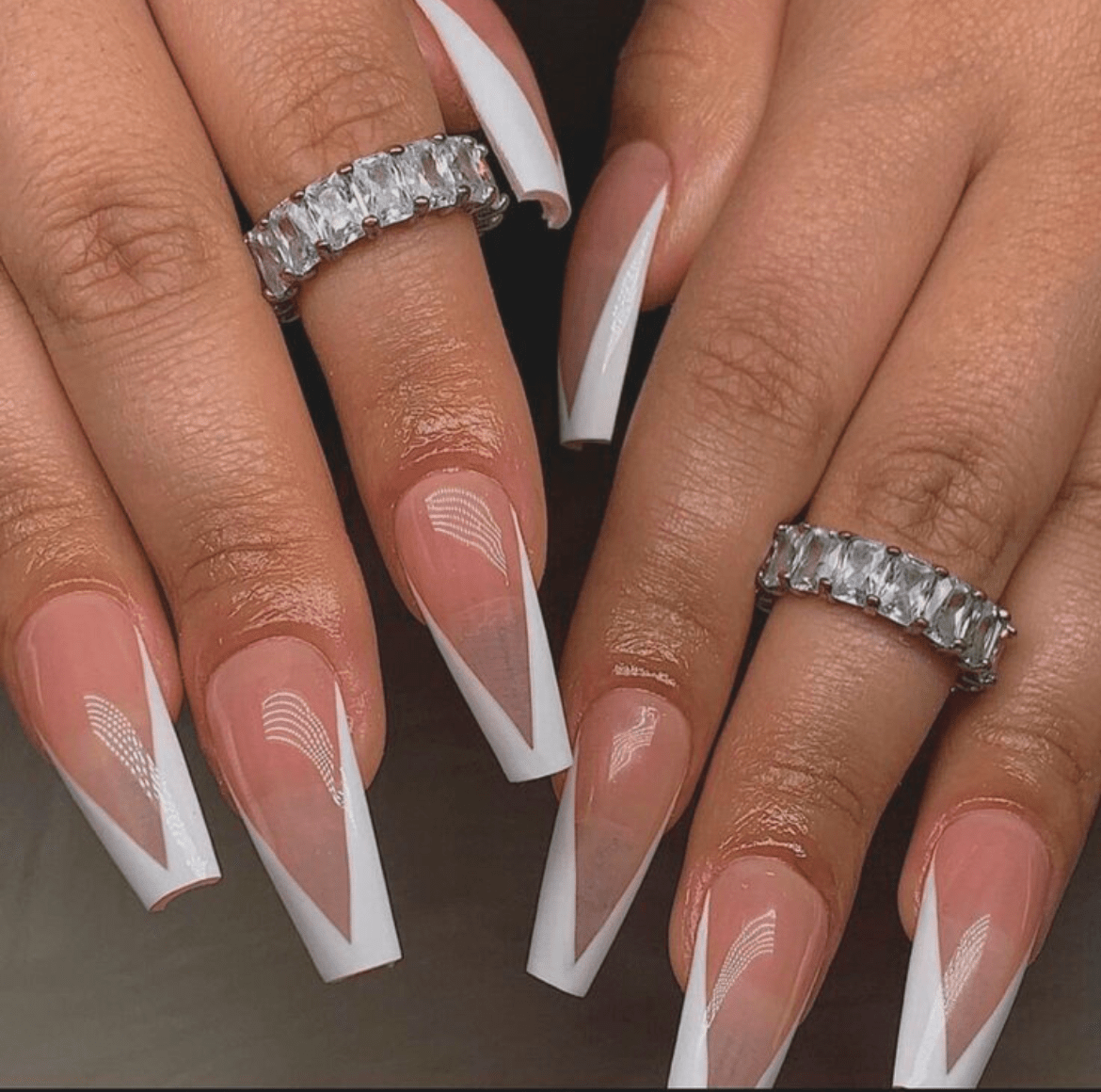 Clear V-shaped nails with sharp white French tips and translucent overlay, accented by diamond-studded silver rings