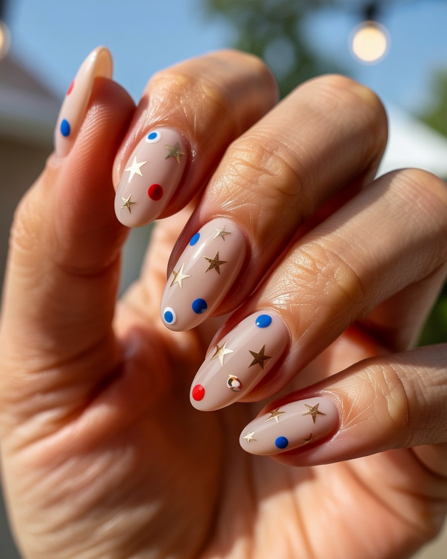 Neutral almond nails with delicate gold stars and red and blue dots for festive summer style.