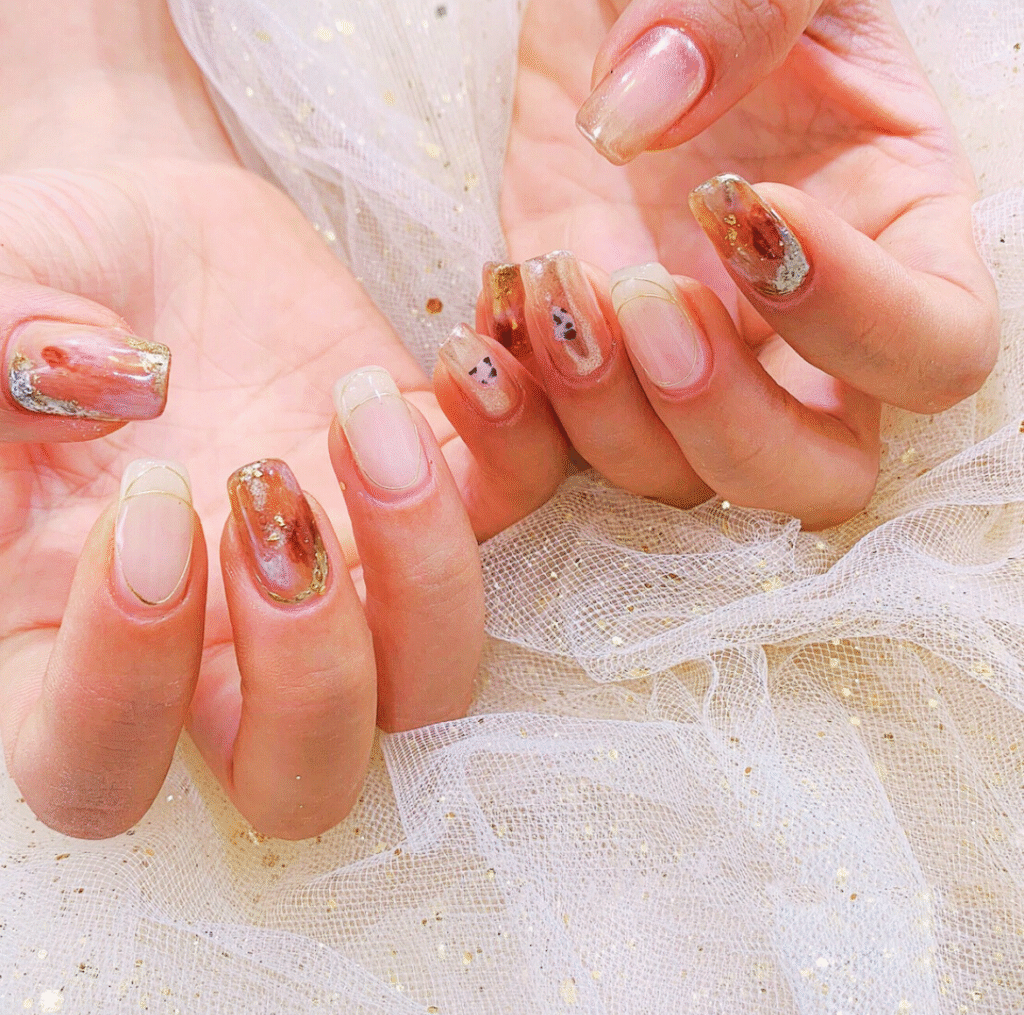 Japanese Minimalist Ombre Nail Style featuring light pink and clear nails with gold flakes, rustic brown accents, and delicate linear gold detailing for a refined, understated look