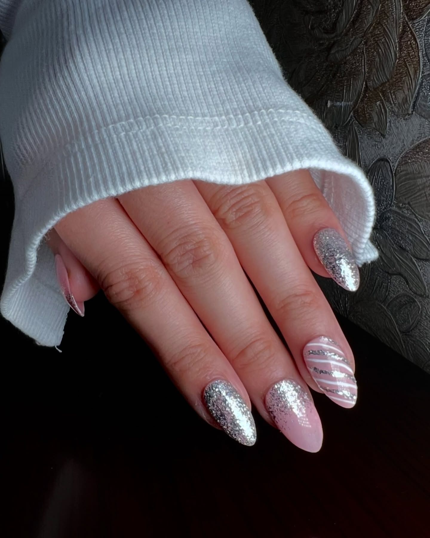 Almond-shaped nails with light pink glitter polish and silver accents, including diagonal stripes and abstract designs

