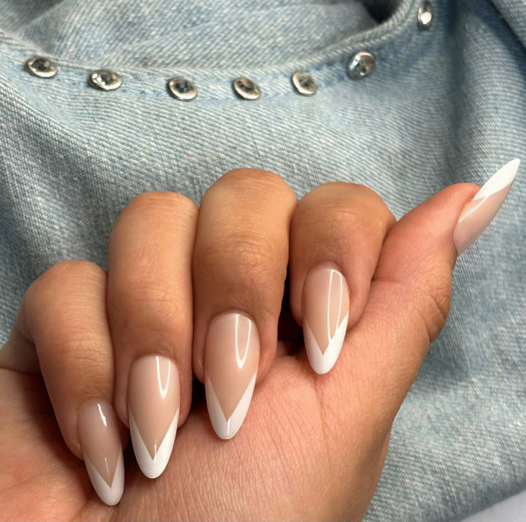 Natural V-shaped nails with glossy nude base and double white V tips against denim fabric with metallic buttons