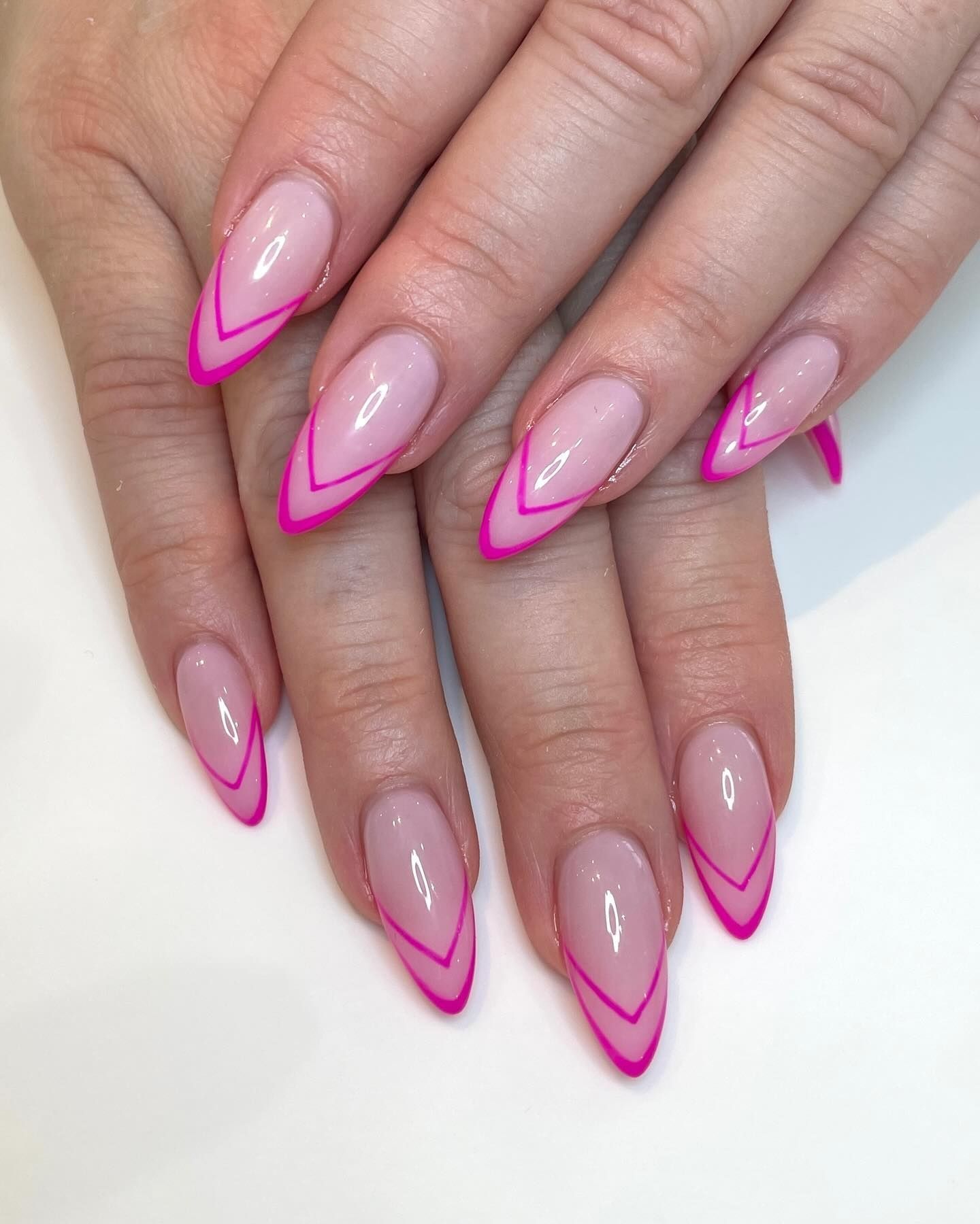Stiletto V-shaped nails with clear base and hot pink V tips in a glossy finish