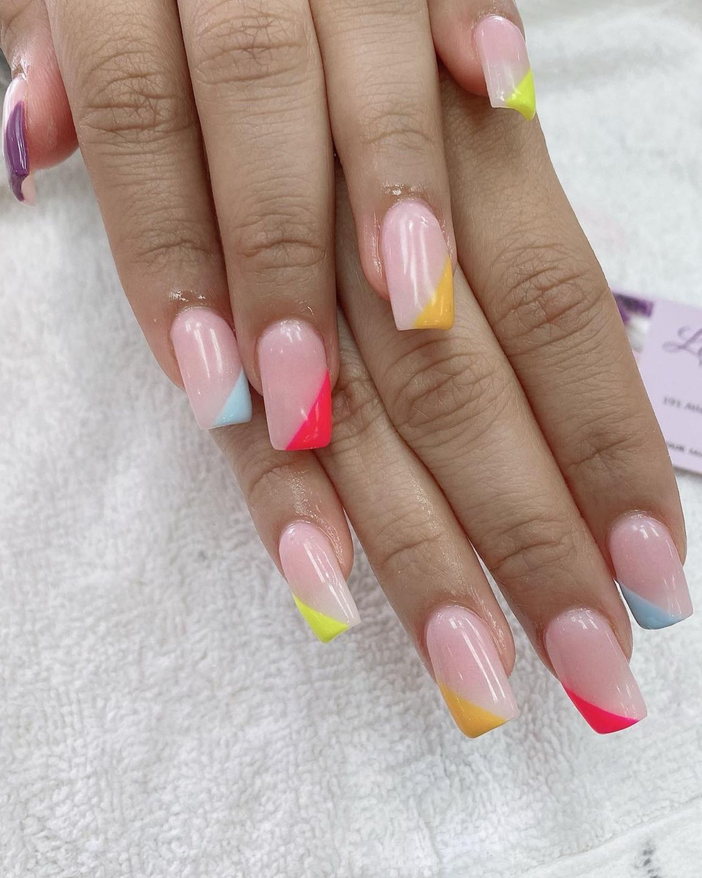 Clear nails with rainbow French tips in purple, neon yellow, pink, and blue, with diagonal color stripes for a vibrant, playful design