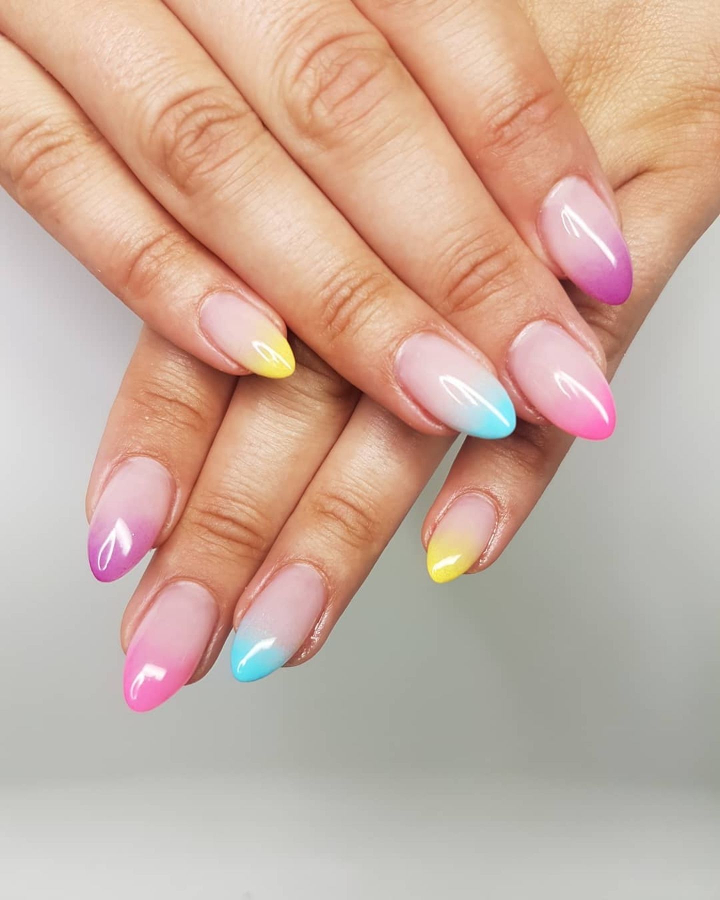 Rainbow Ombre Nails with almond-shaped nails transitioning from pink at the base to blue and yellow at the tips for a smooth, vibrant gradient effect