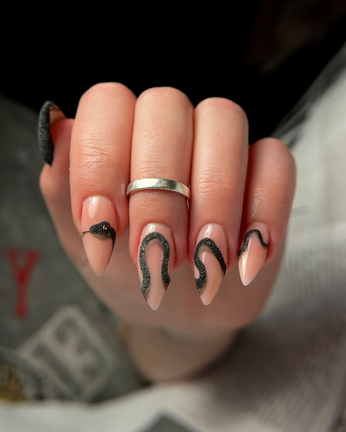 Snake Pattern Nail Design with almond-shaped nails in soft pastel peach, featuring black snake motifs and glitter accents for an edgy, minimalist look