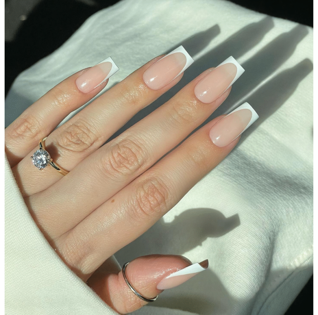 Long square nails with natural French tips, showcasing a solitaire diamond engagement ring and silver open-ended ring for an elegant, modern look
