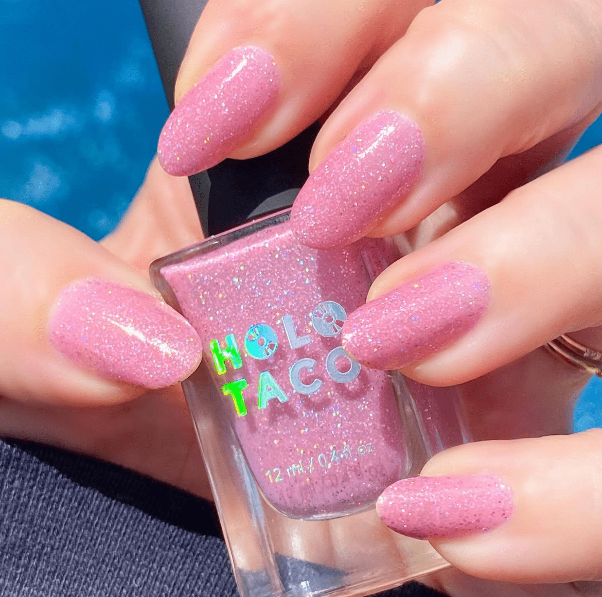 Hand with blush holographic almond nails holding a Holo Taco nail polish bottle