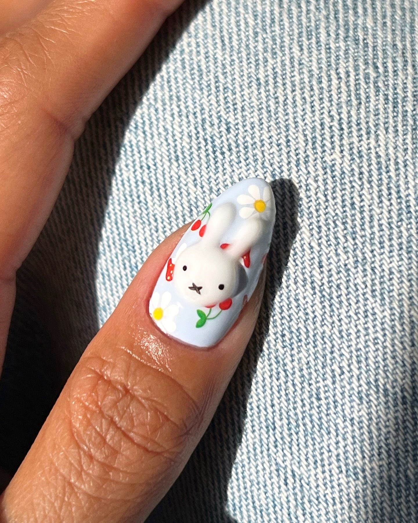 Almond-shaped blue nail with 3D white bunny, hand-painted daisies, and strawberries for a whimsical spring design