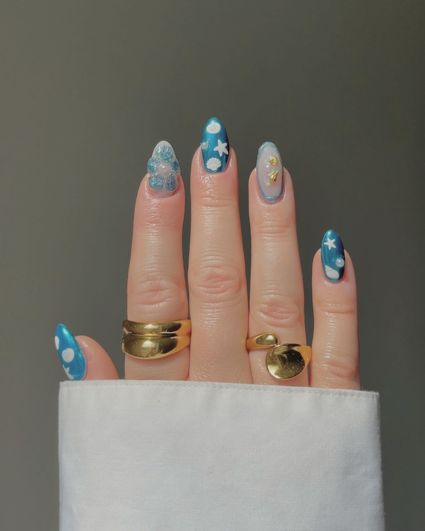 Hand with chrome-inspired summer nails in various blue designs, featuring flowers, starfish, and goldfish accents with glossy finish