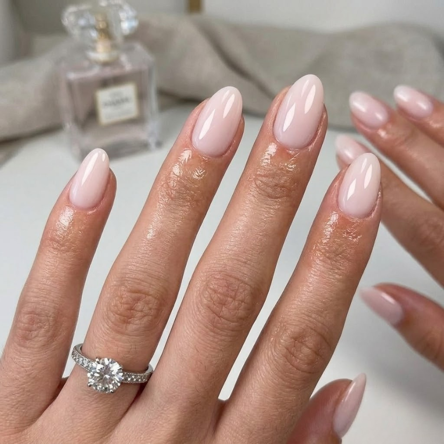 Oval-shaped pale pink nails with a sheer milky finish on ivory linen background
