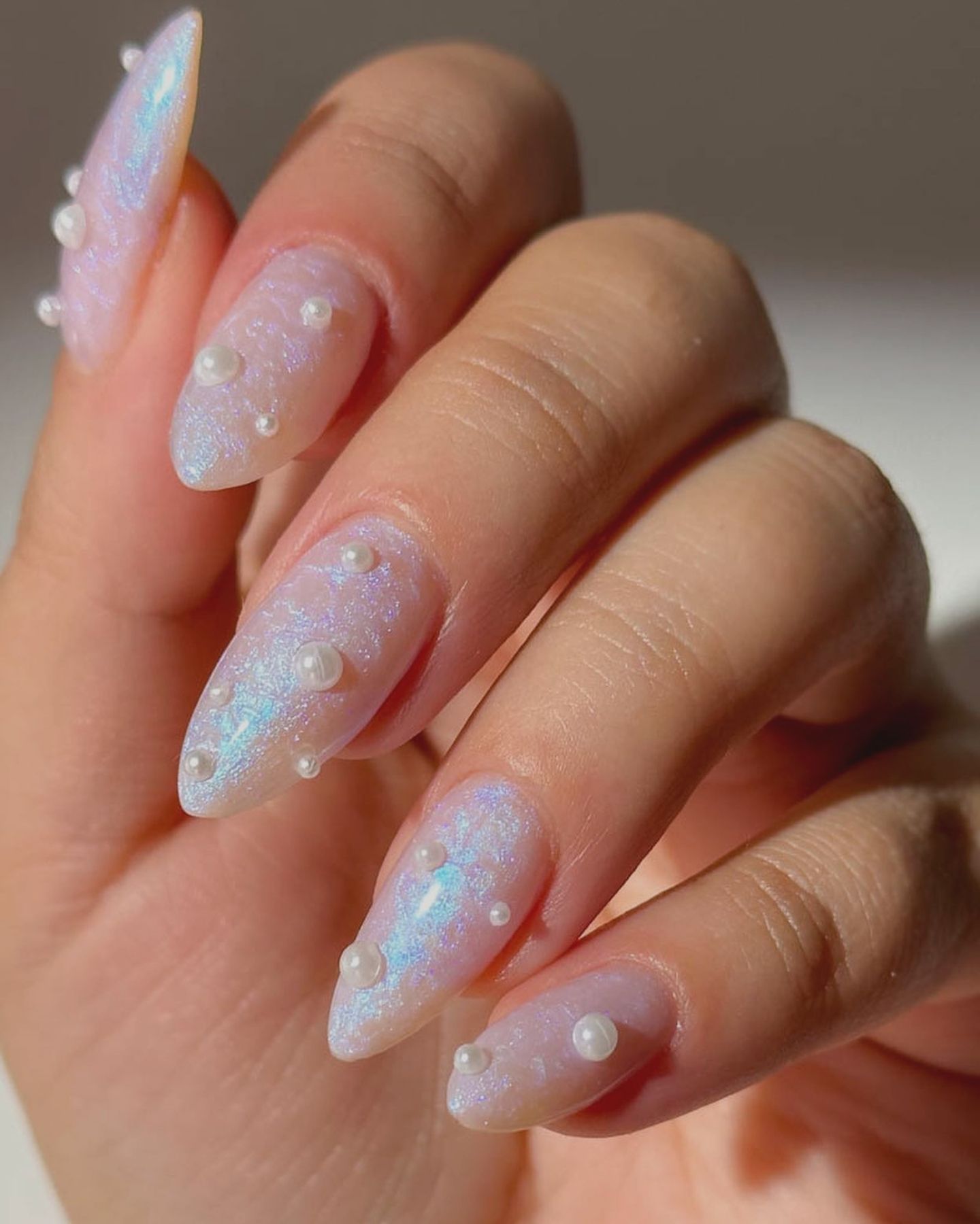 Stiletto-shaped blue nails with pearl accents and sparkly holographic finish