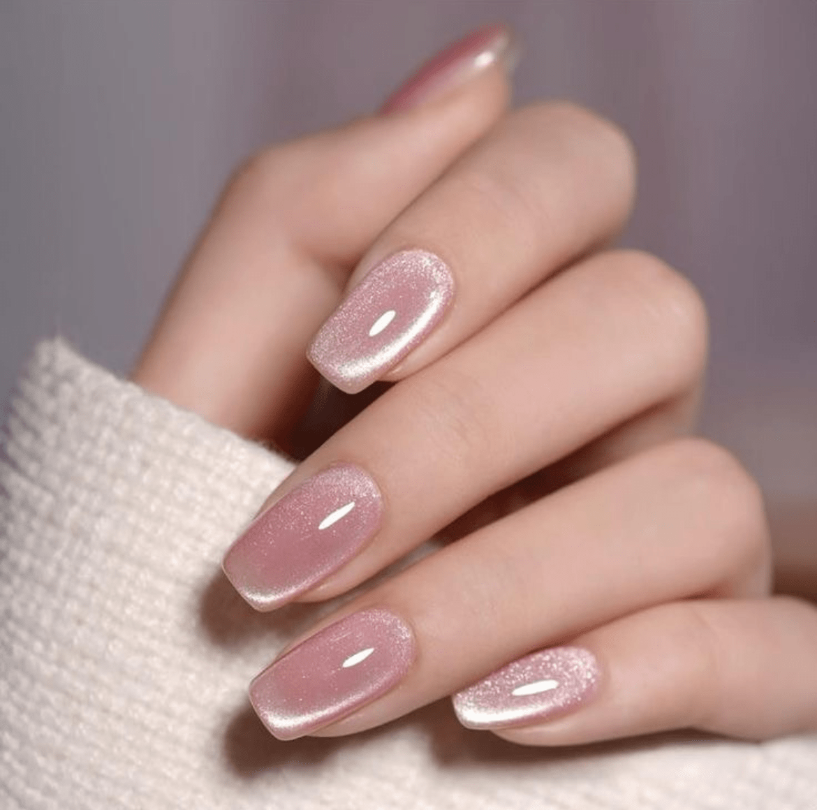 Close-up of pink cat eye nails with a soft shimmer, fingers curled on a textured knit fabric background.

