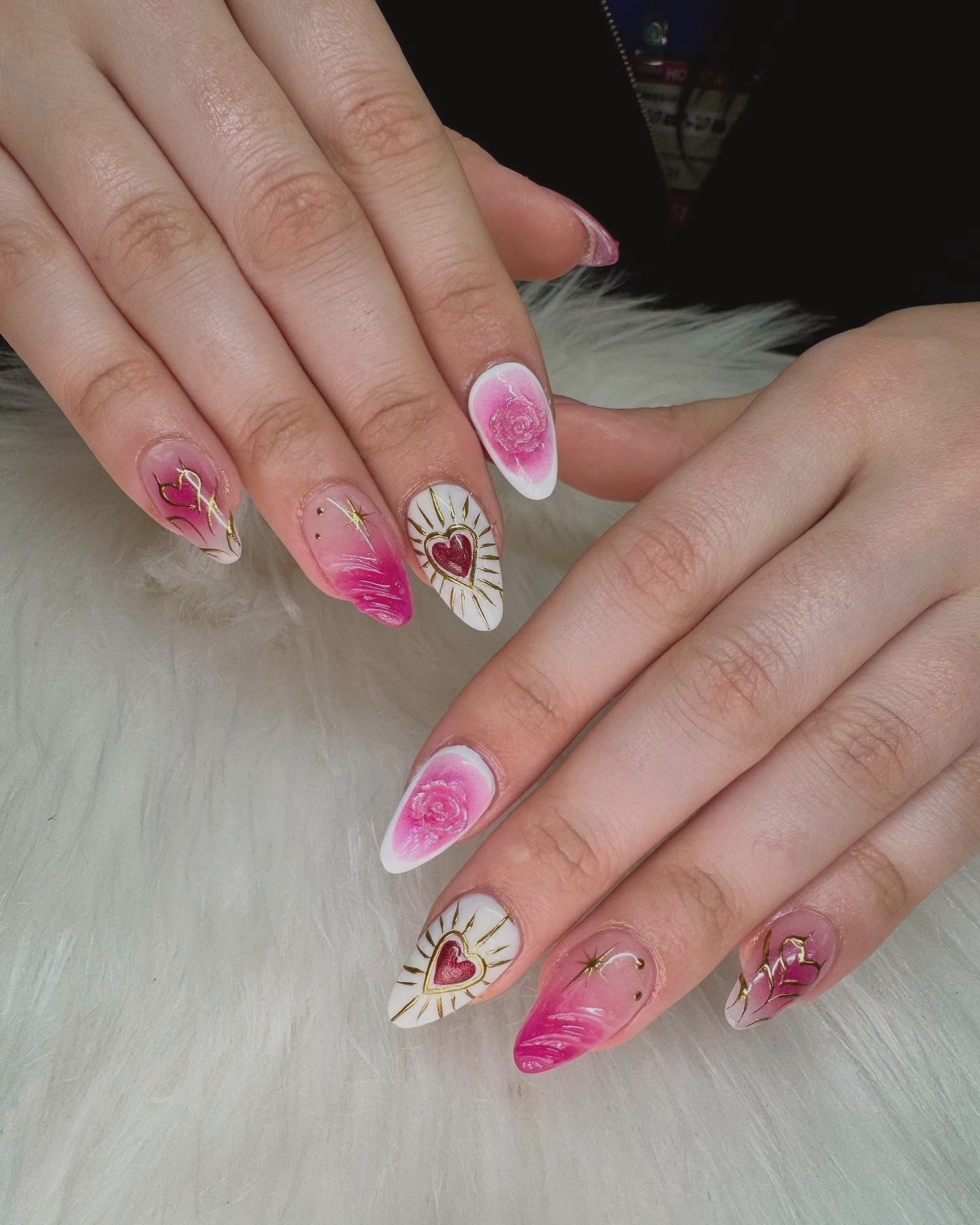 Pink gradient nails with gold accents and heart design, styled on a soft white background for a romantic Valentine’s Day look.
