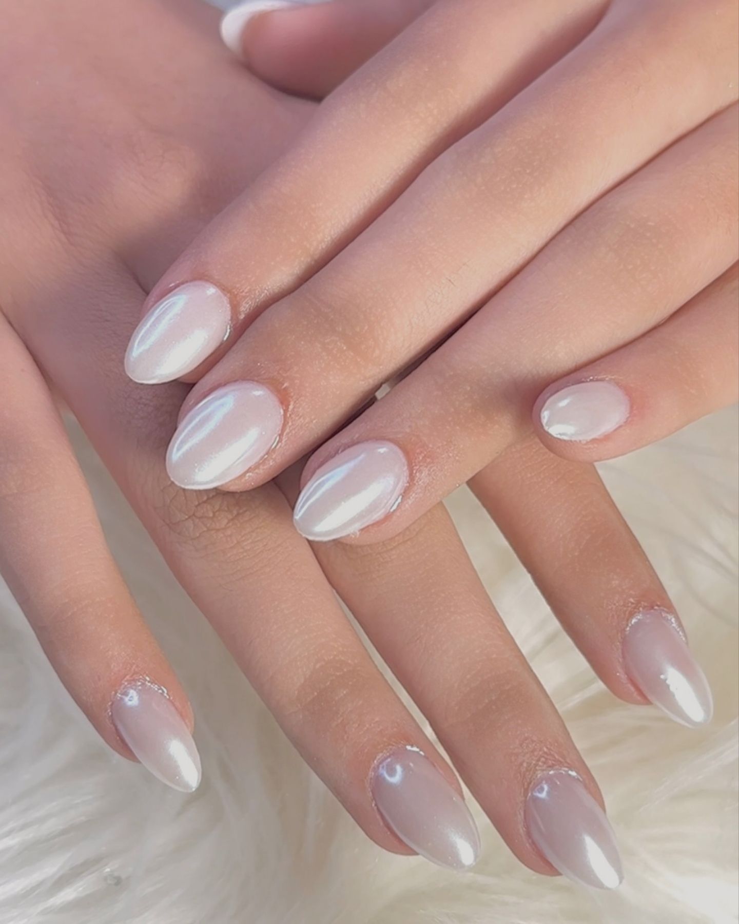 Almond-shaped nails with pale chrome polish and silver flakes, set against a soft white background
