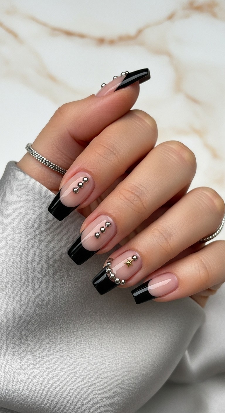 Almond nails with glossy black French tips and tiny silver stud accents, gold star detail on ring finger, gray silk background
