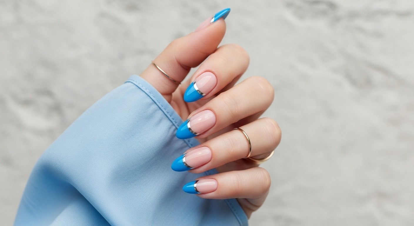 Almond-shaped Blue French tip nails with silver stripes, shown on a naturally posed hand wearing a soft blue sleeve and delicate gold ring, against a textured light grey background.