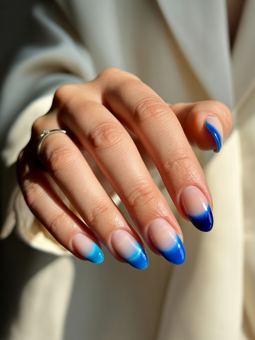 Hand with glossy French gradient nails in multiple blue shades, clearly visible with soft lighting and a neutral background.

