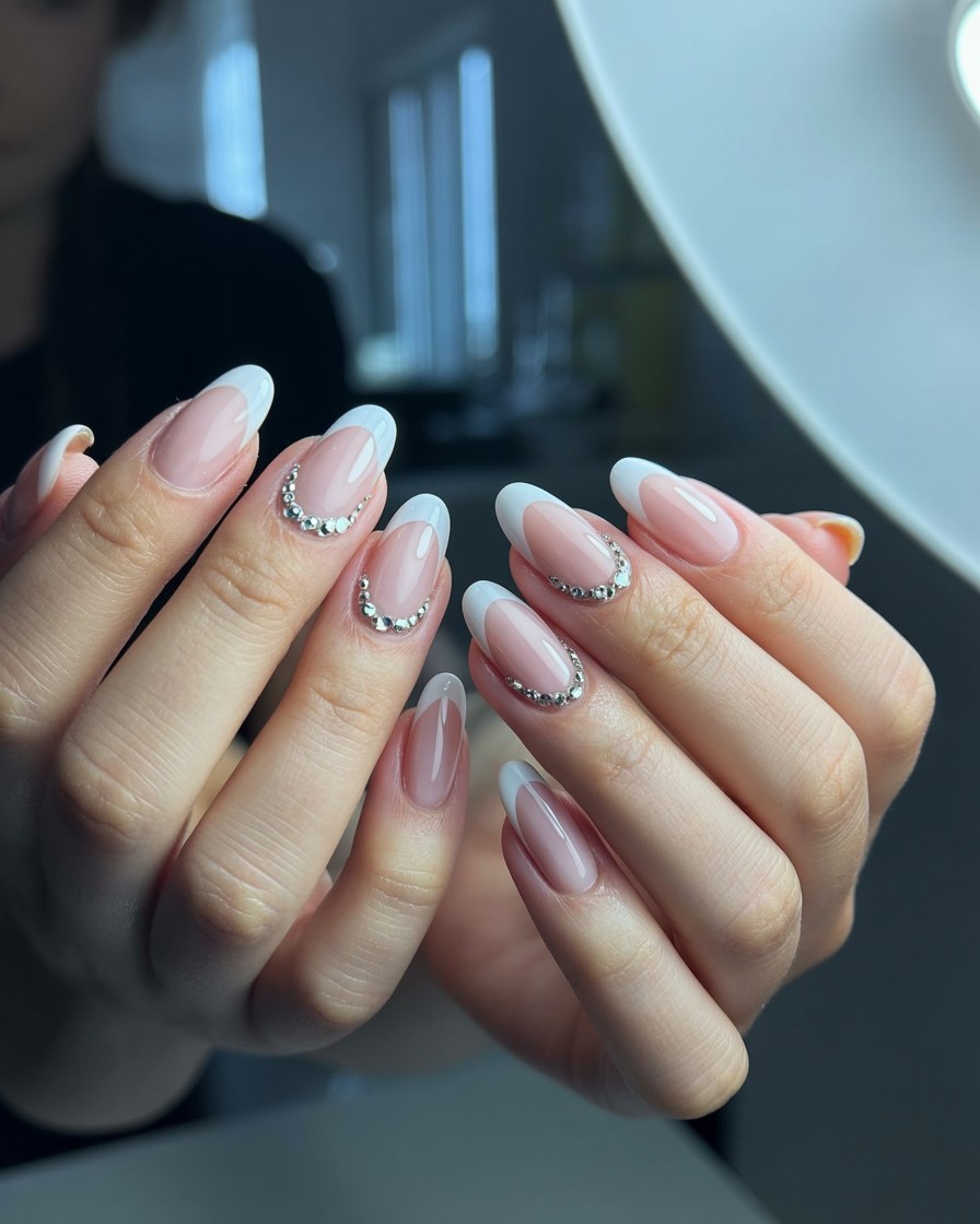 White French tip nails with sparkling diamond-shaped rhinestone accents on glossy square-shaped nails in a modern nail salon setting.