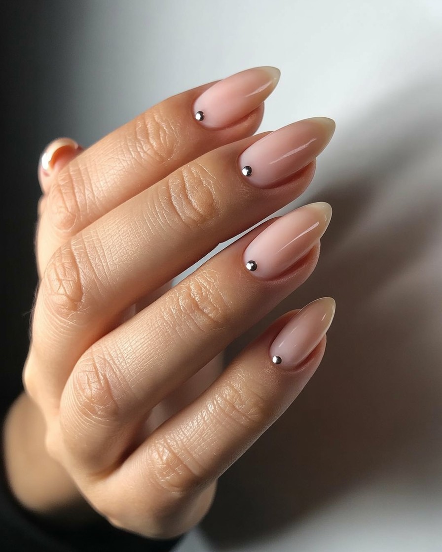 Whole hand with glossy nude nails featuring single chrome dot accents on each nail.