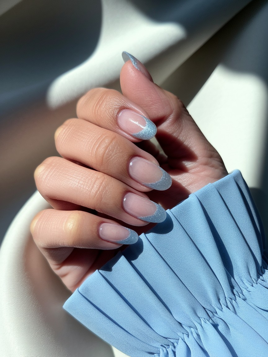 Side view of hand with glossy nails featuring ice blue shimmer tips, paired with a light blue summer dress sleeve.

