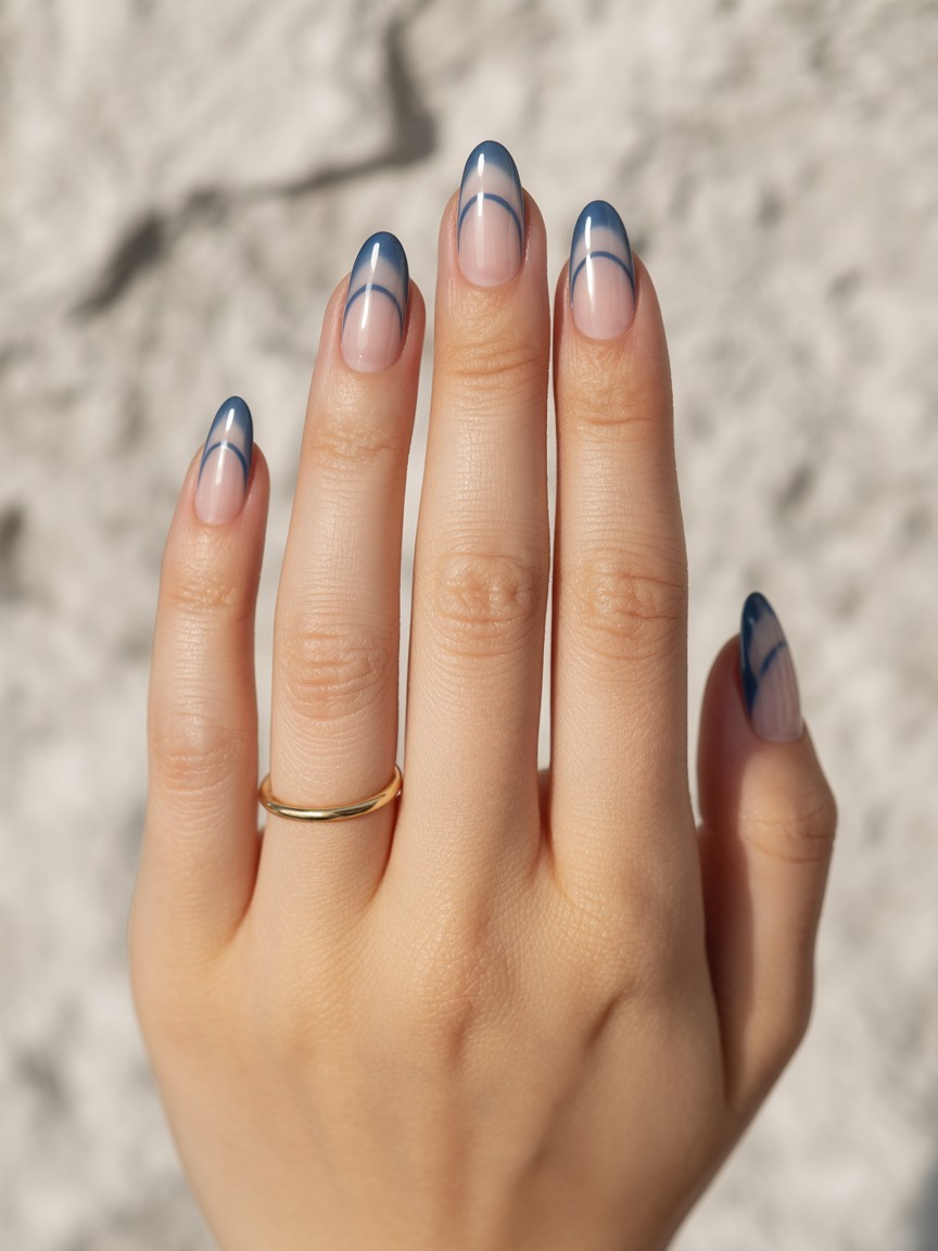 Almond-shaped nails with indigo ombre curve design, back of hand view with glossy finish and minimal gold ring.

