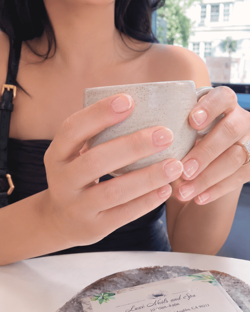 Short natural nails with ultra-thin white French tips on a sheer nude base, creating a clean and minimalist June manicure.