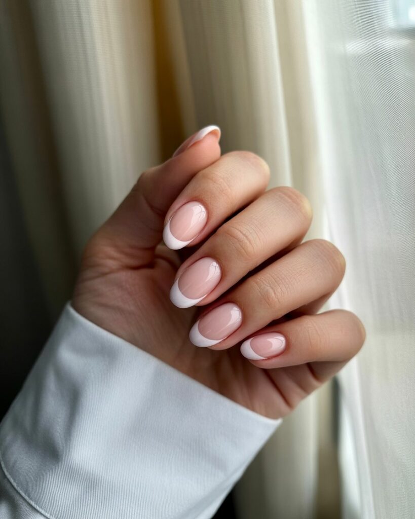 Close-up of almond-shaped nails with sheer nude base and slim white French tips, glossy finish, natural and elegant manicure.