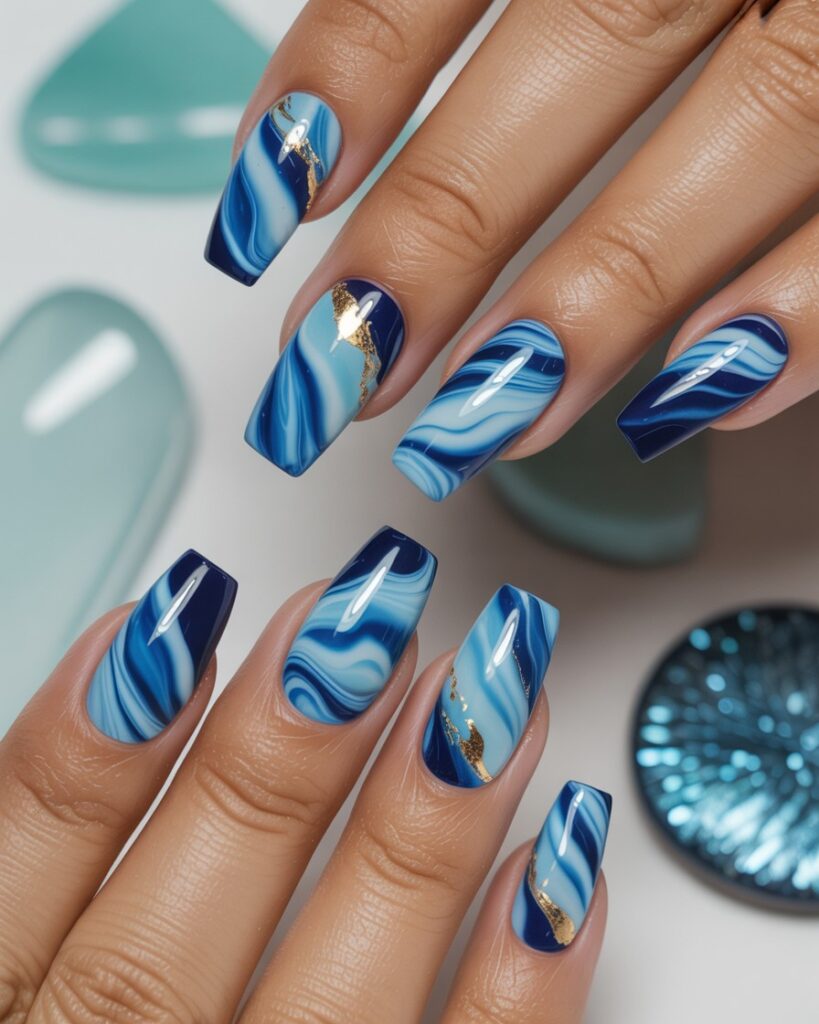 Glossy marbled blue swirl nails with gold foil accents, inspired by ocean waves.