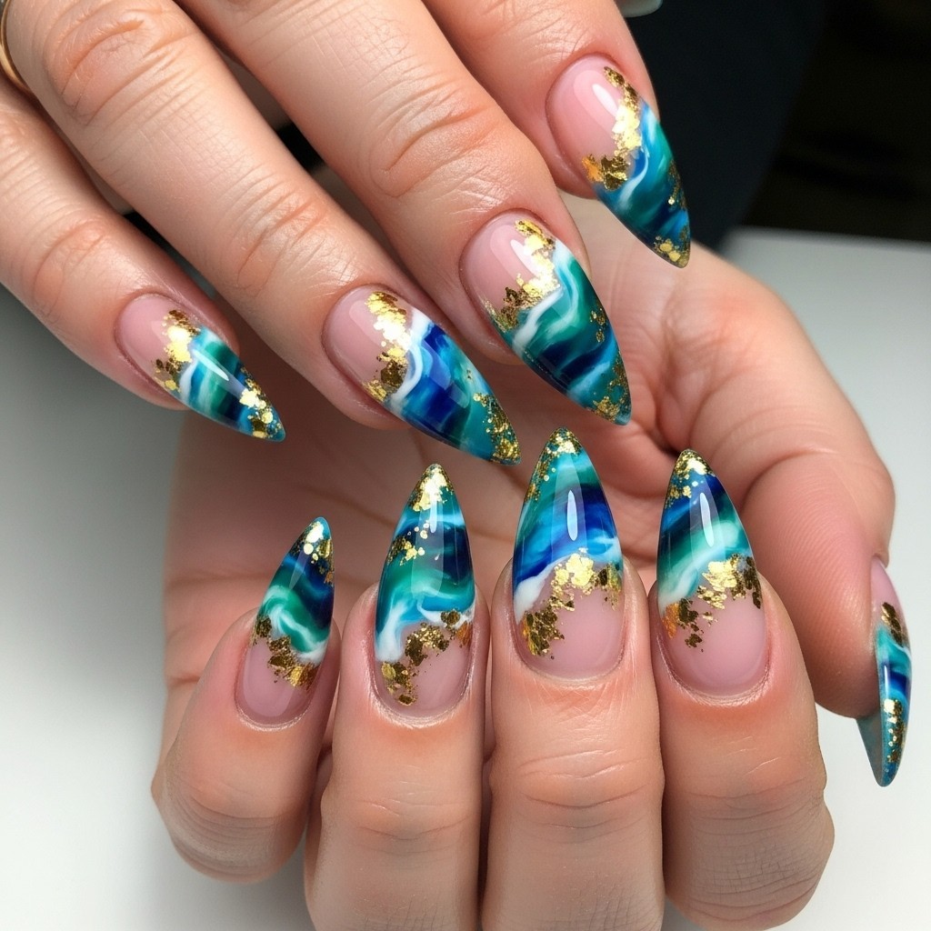 long stiletto nails featuring an ocean wave chrome design with marbled teal, blue, and white polish, light pink bases, and scattered gold flakes for a shimmering effect.