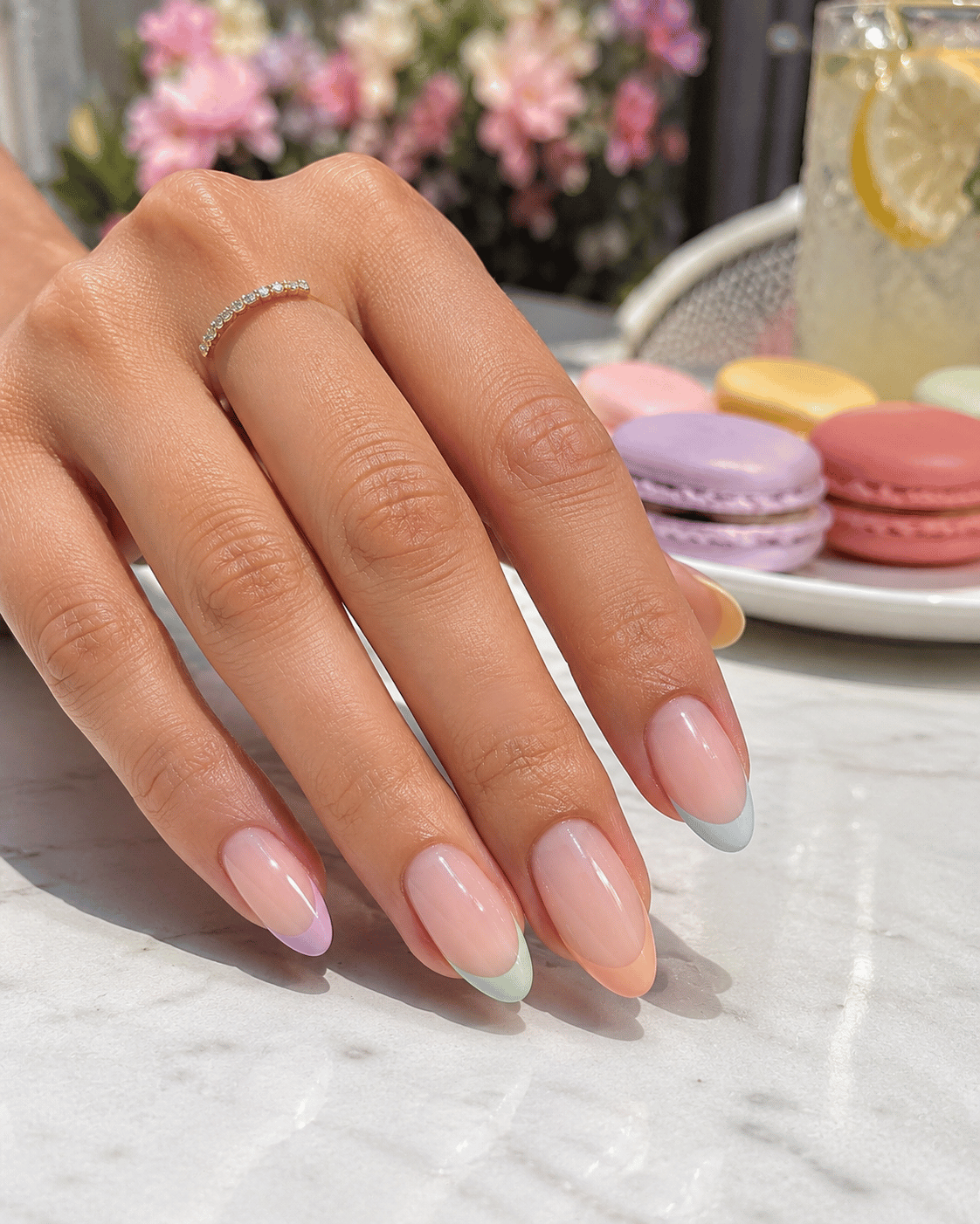 Pastel rainbow French tip manicure with lavender, mint, peach, baby blue, and butter yellow tips on glossy almond-shaped nails at a summer café setting.