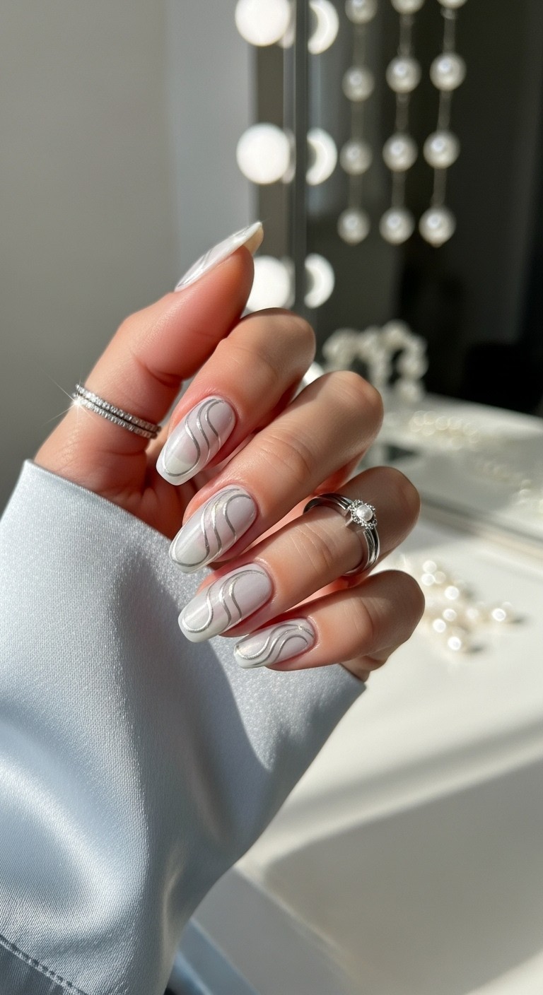 Pearly White Swirl French manicure with opalescent white base and silver swirl designs on oval nails, styled with platinum jewelry against blue silk background.