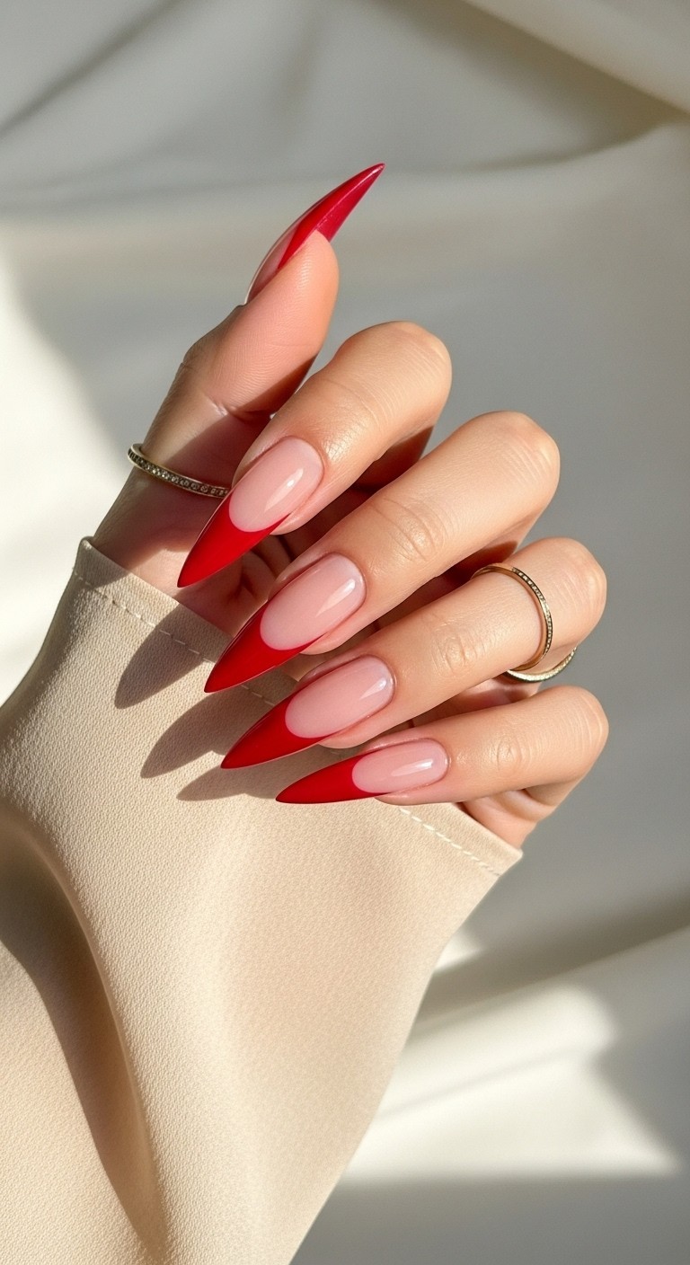 Long stiletto nails with glossy red French tips on a sheer nude base, styled with a delicate gold ring and soft chiffon sleeve.