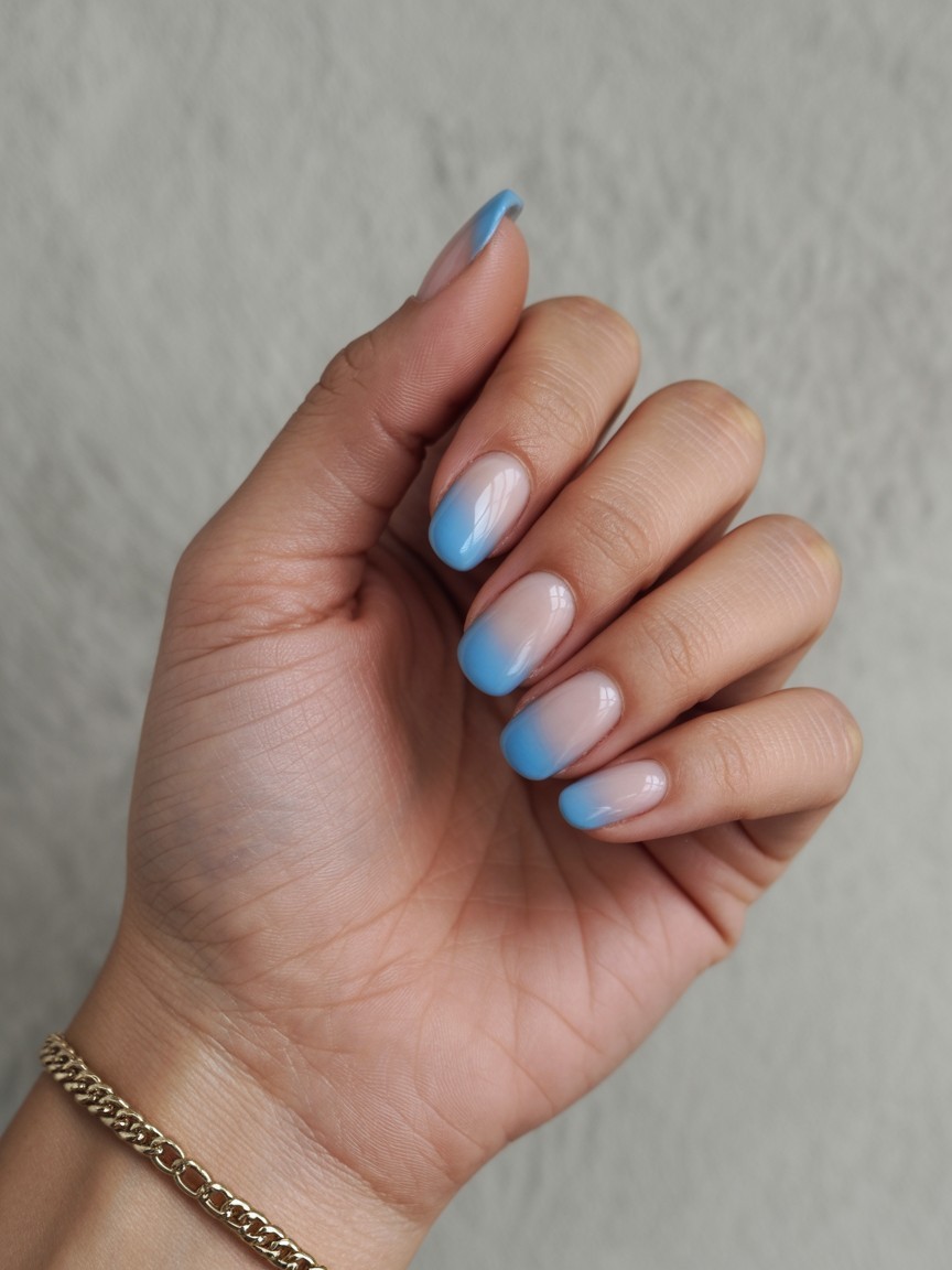 Palm view of hand with sky blue French fade nails, glossy finish and soft gradient tips, resting on pale stone with a delicate gold bracelet.