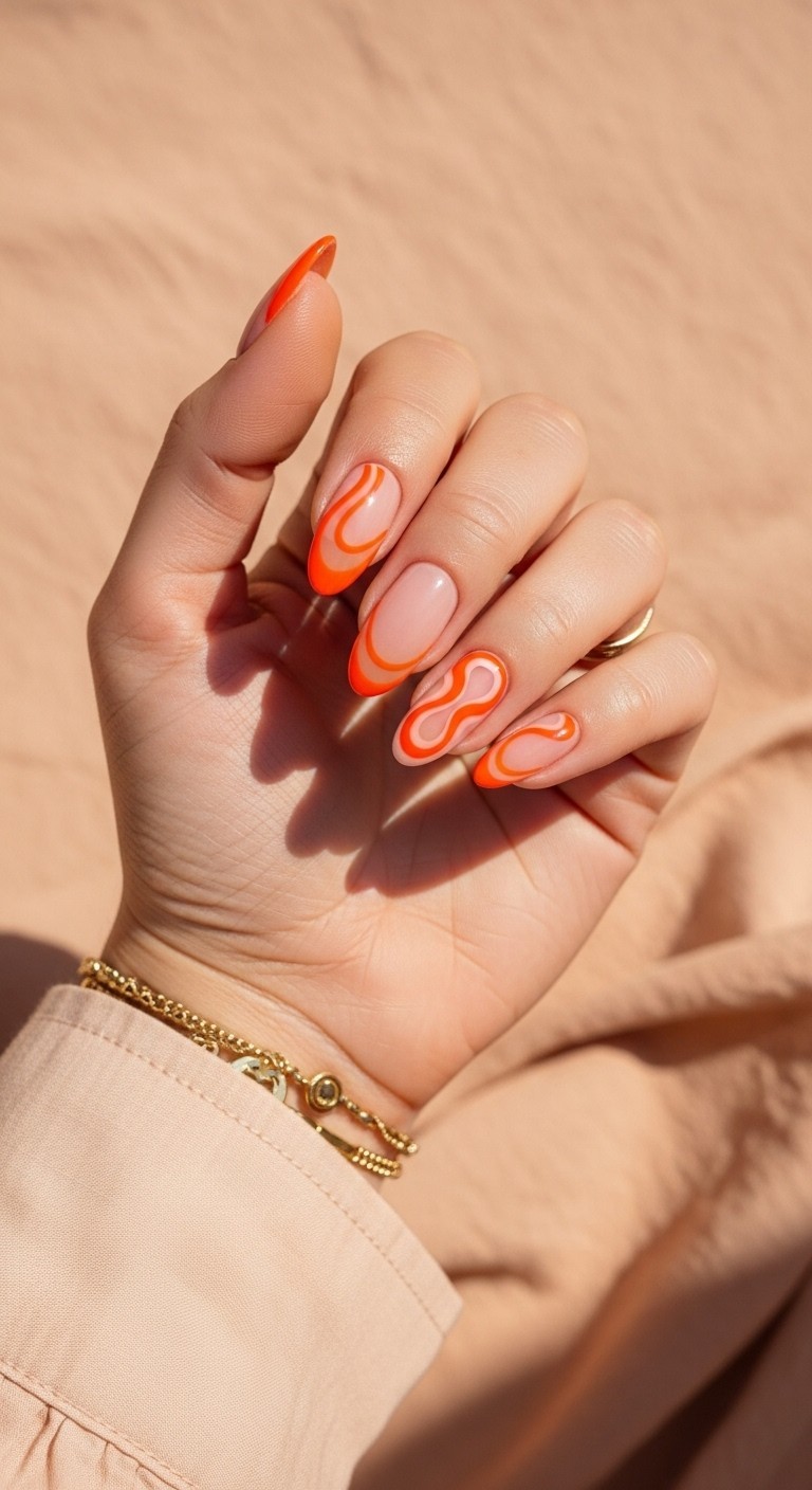 Manicured hand with tangerine swirl French tips on nude base, featuring vibrant orange curves and gold accessories against a peach-toned background.