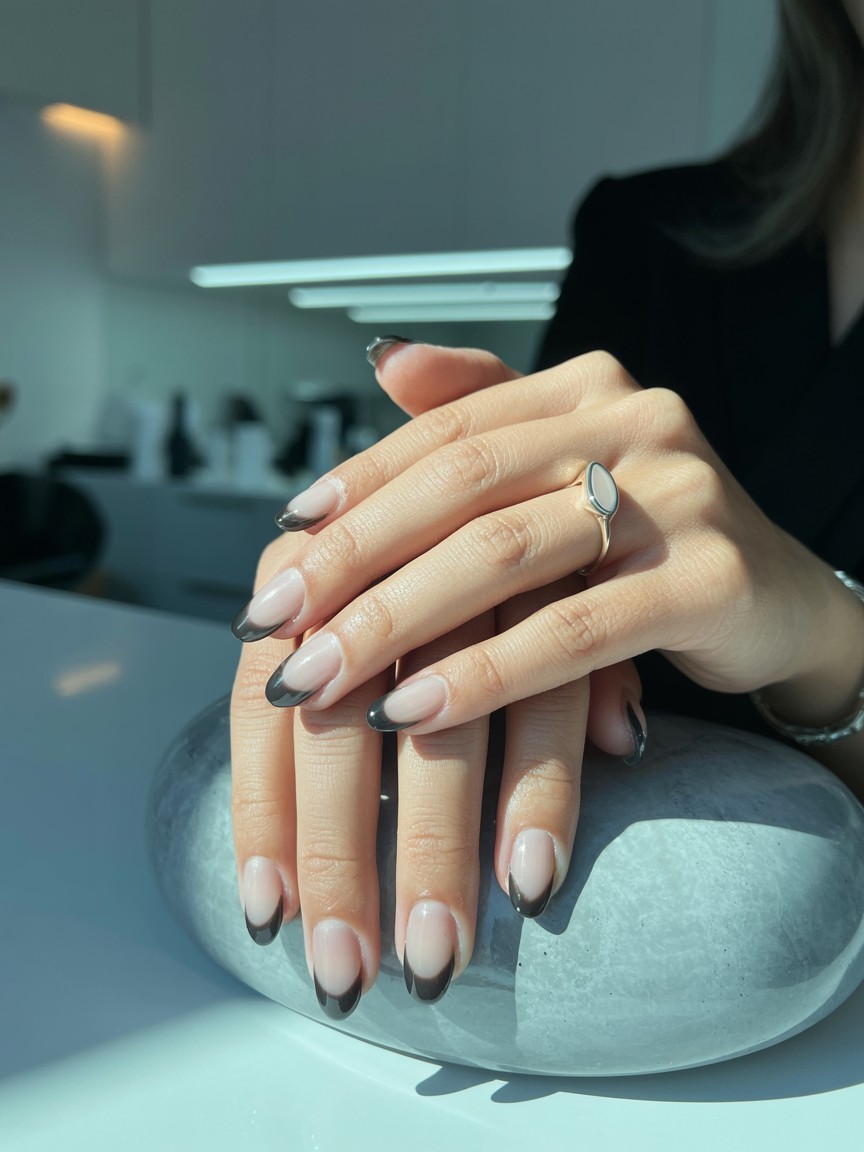 Close-up of hand with translucent black French tips over a sheer base, accessorized with rings in a modern nail salon setting.