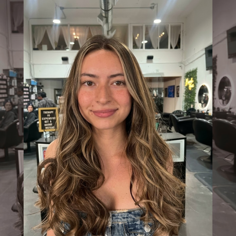 Golden caramel balayage on dark brown hair styled in soft waves inside a real salon with natural lighting