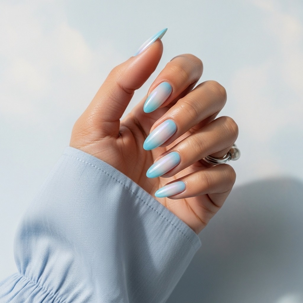 Natural hand with sky blue aura nail art on a nude base, styled with a light summer sleeve and soft lighting on a neutral background.