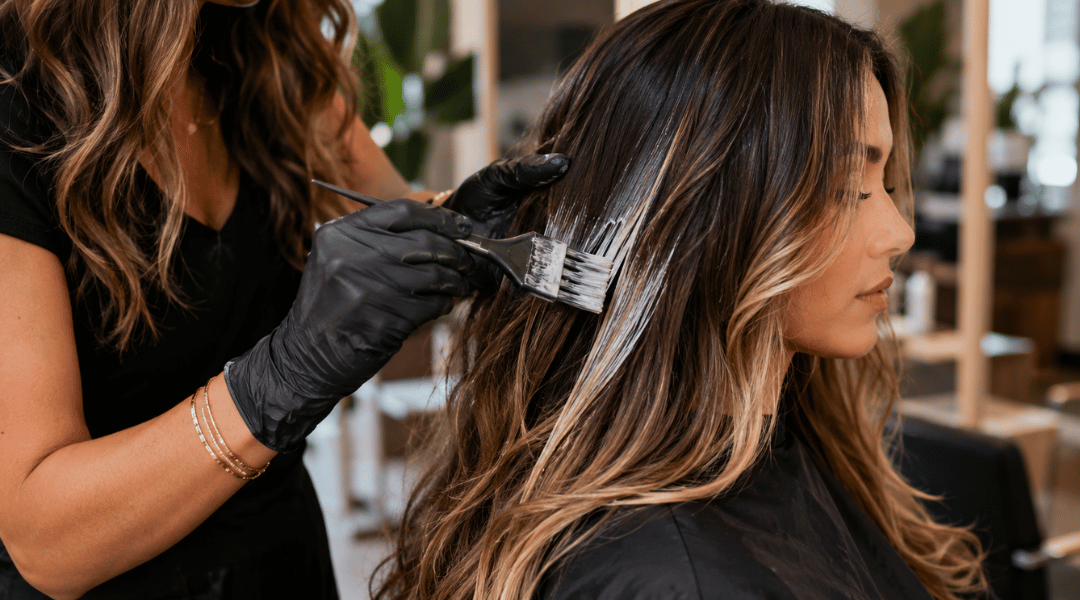 Stylist hand-painting balayage highlights onto brunette hair to create natural-looking dimension and a sun-kissed effect.