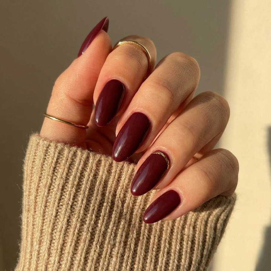 Burgundy Christmas nail with a subtle gold accent, styled in a natural salon setting for an elegant holiday manicure