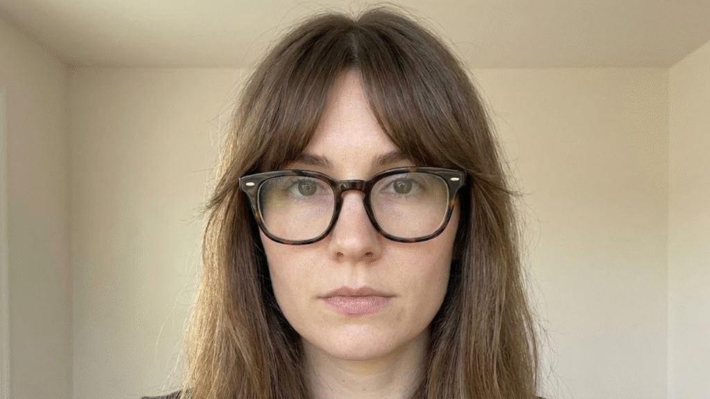 Woman with thin hair wearing thick glasses and open split bangs, showing how avoiding blunt lines prevents horizontal stacking at the mid-face.