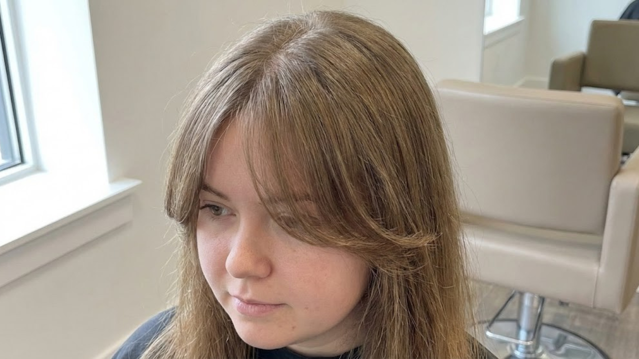 Side-swept curtain bangs on a round face with thin hair, showing diagonal flow that pulls the eye vertically and reduces visible scalp without requiring bulk.