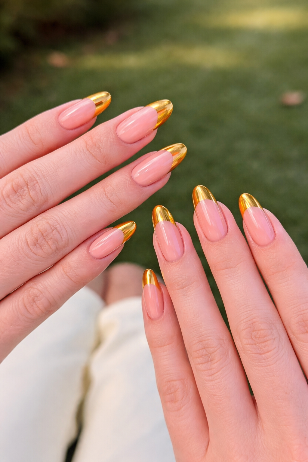 Gold chrome french tip nails on almond shaped nails with a nude base in natural outdoor lighting