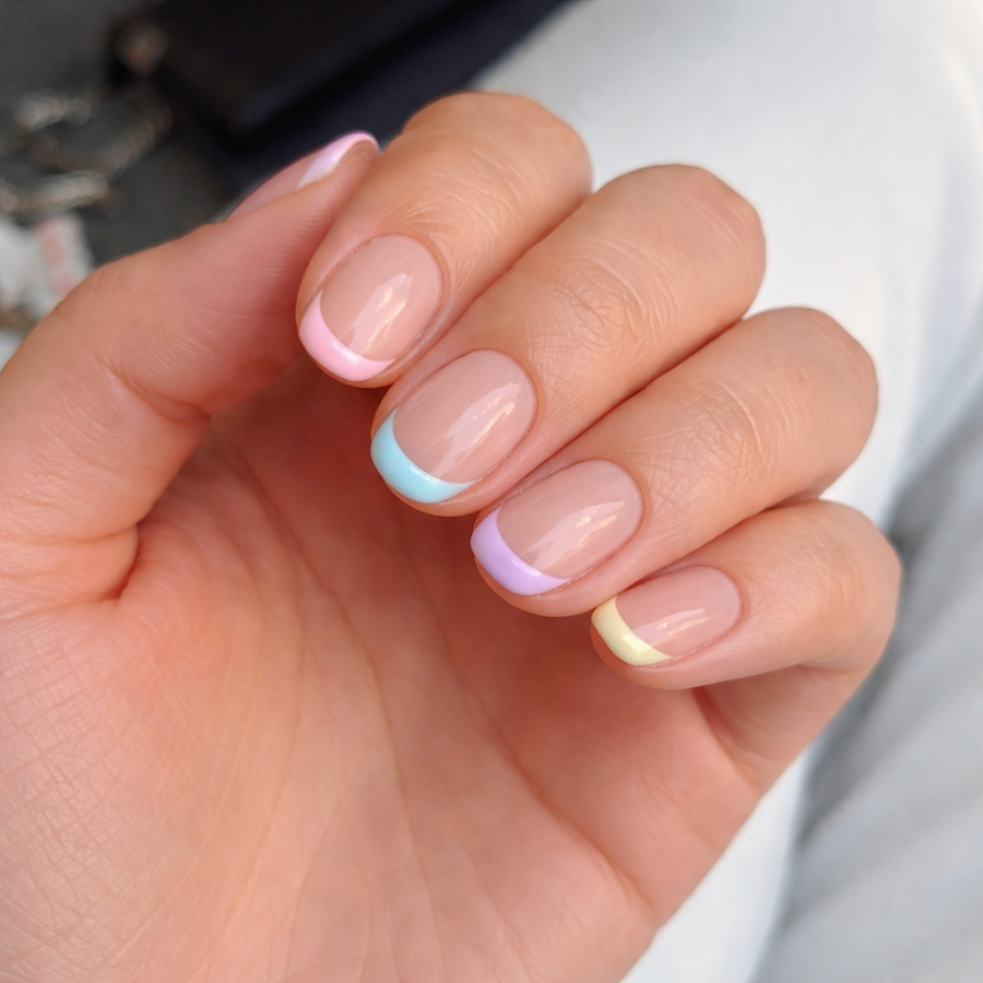 Short french tip nails with thin pastel colored tips on a natural nude base showing a soft multicolor design