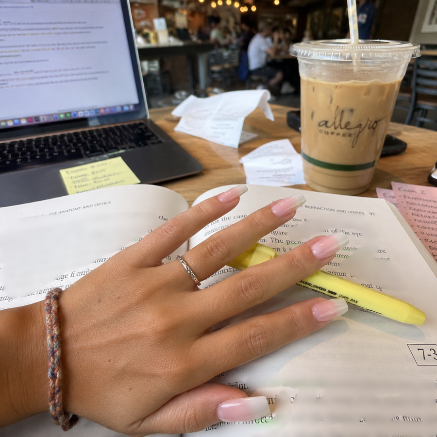 Pink and white bubble bath ombre coffin nails resting on an open textbook in a coffee shop with a yellow highlighter, iced coffee, and laptop in the background.