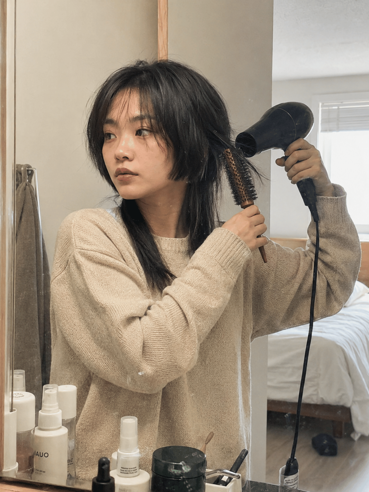 Woman styling a jellyfish haircut with a round brush and blow dryer to maintain the separation between the short top layer and longer bottom layer.